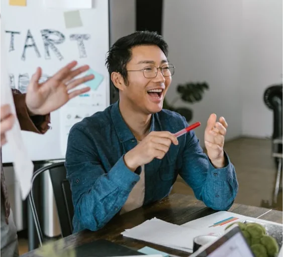 Smiling businessman in glasses holding a pen during a team meeting, engaged in creative brainstorming at the office.