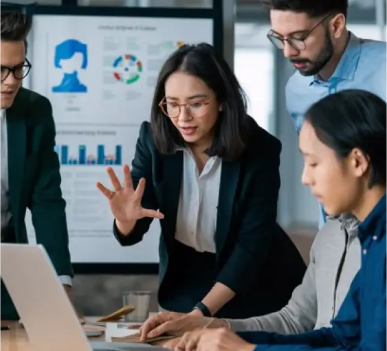 Diverse business team analyzing data and discussing strategies around a laptop with charts and graphs in the background.